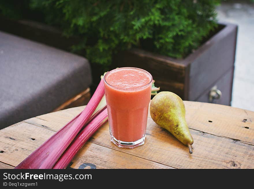 A fruit smoothie with rhubarb stalks and pear next to it.