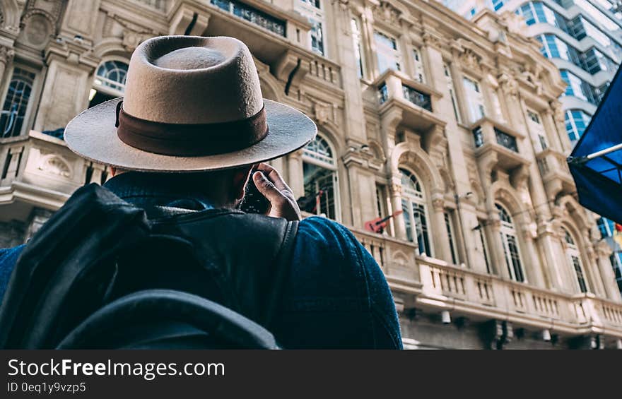 Man in Beige Hat Taking Picture on Beqige Conrete Architectural Building