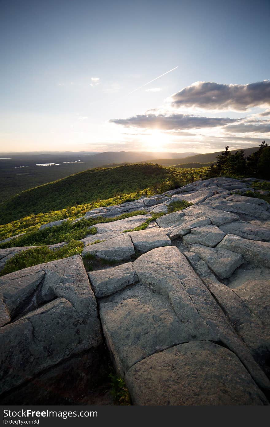 Sunset over the Horizon Surrounded by Green Mountains on a Clear Blue Sky