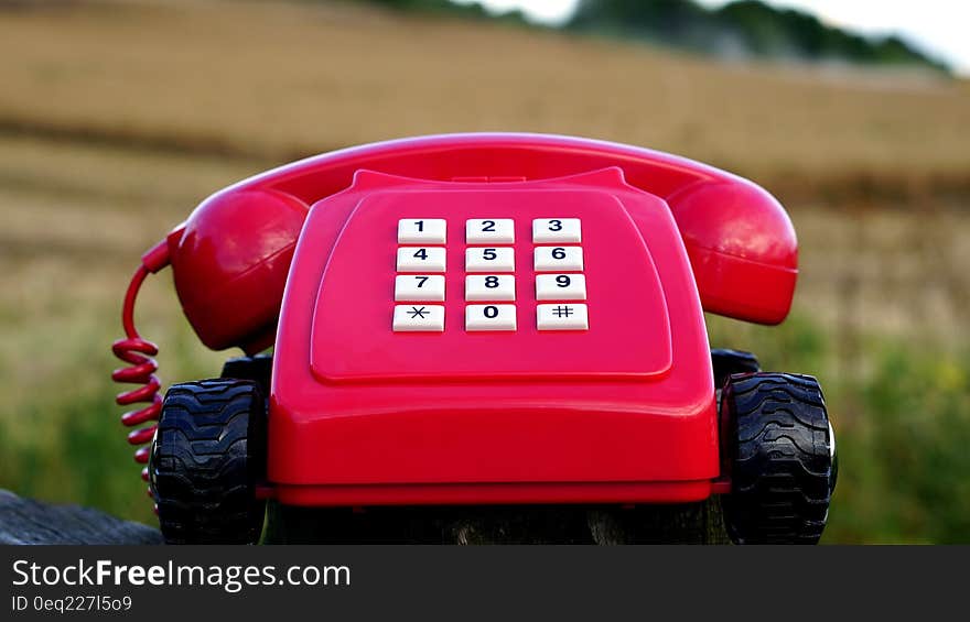 Red Rotary Phone With Black Wheels Near Brown Grasses during Day Time