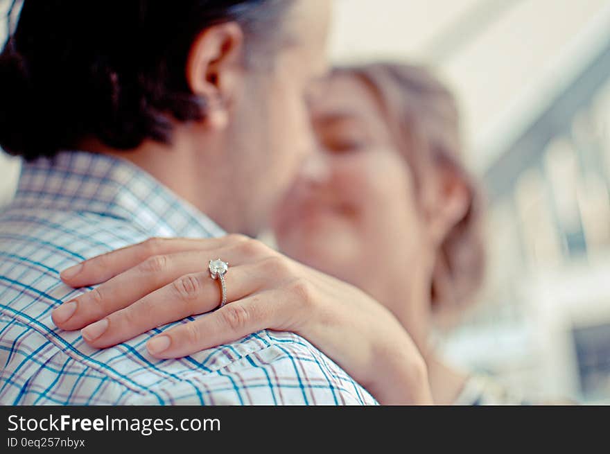 Closeup of couple having a hug but with selective focus on a diamond ring on the woman's finger and their faces are blurred.