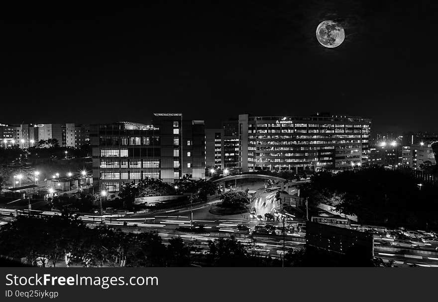 A black and white photo of full moon above city.