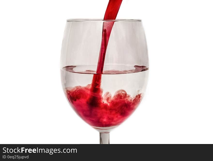 Pouring red soda into a glass with transparent liquid inside.