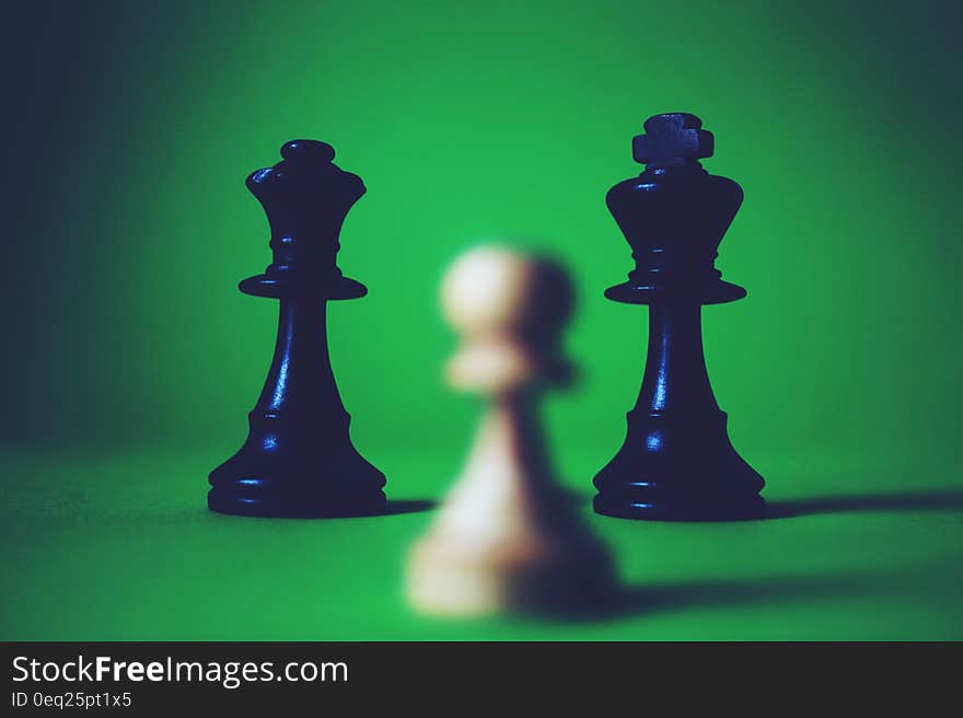 Close up of black queen and king chess pieces with white pawn on green background. Close up of black queen and king chess pieces with white pawn on green background.