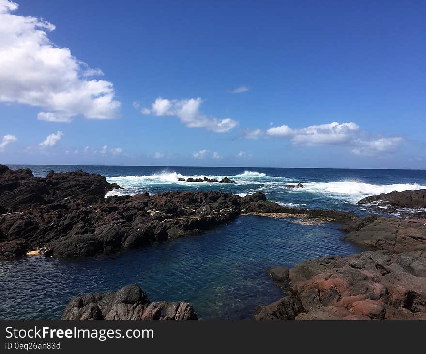 Brown Rocks Beside Ocean With Bubble Wave Under Blue Sky