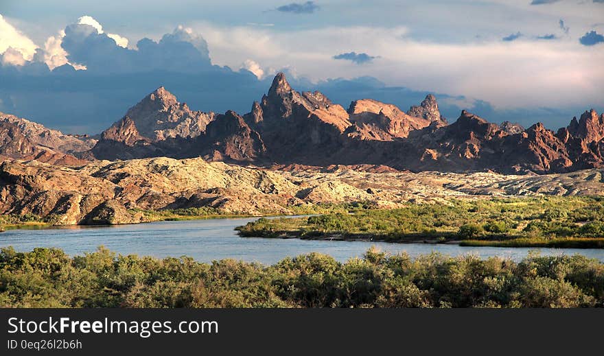 Brown Mountain Beside Lake Under White Clouds