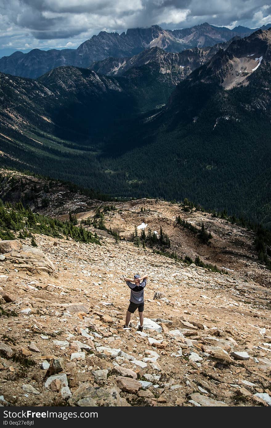 Hiker standing on rocky slopes in mountains under clouds in blue skies with clouds. Hiker standing on rocky slopes in mountains under clouds in blue skies with clouds.