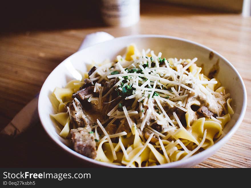 Bowl of pasta noodles with meat and shredded vegetables on wooden table. Bowl of pasta noodles with meat and shredded vegetables on wooden table.