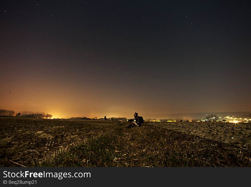 Man sitting on hillside over town illuminated at night. Man sitting on hillside over town illuminated at night.