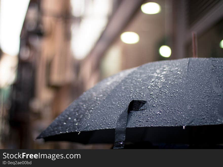 Closeup of umbrella in the rain with selective focus on rain drops, blurred urban background.