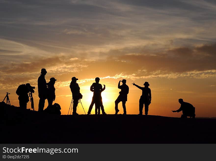 A view of a hill with the silhouettes of people filming and photographing the sunset. A view of a hill with the silhouettes of people filming and photographing the sunset.