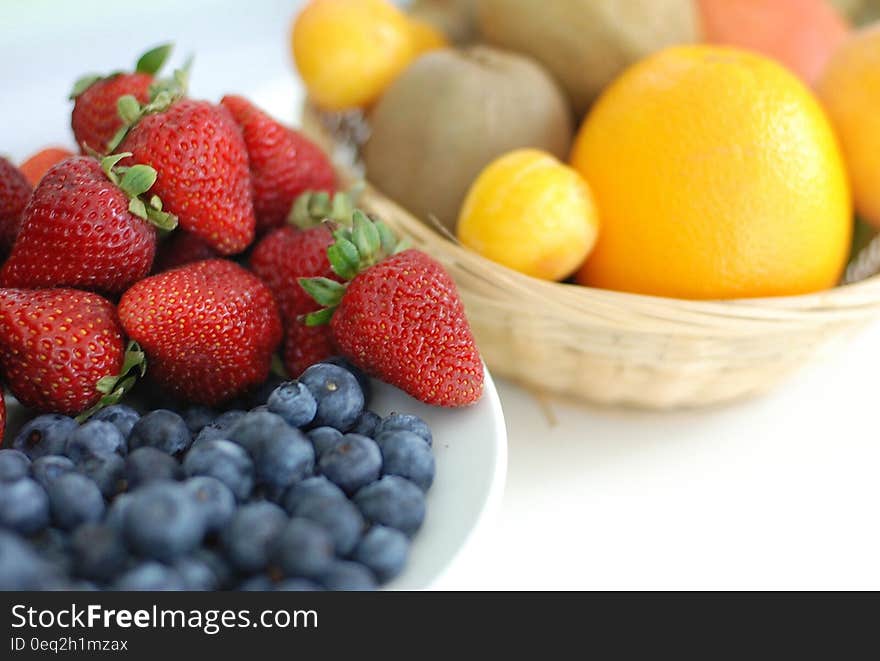 Red Strawberry, Blue Berry on White Plate Near Brown Woven Basket