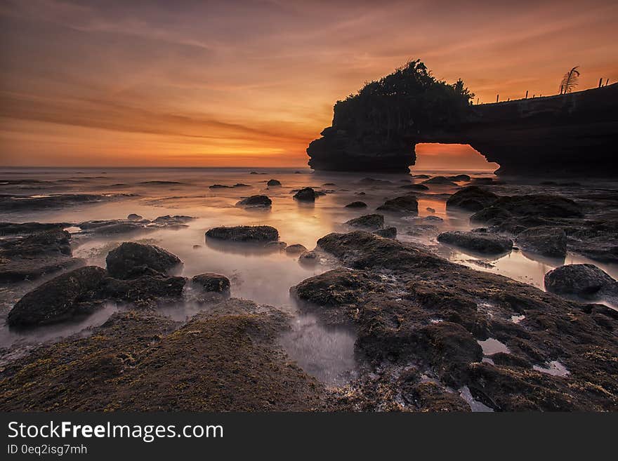 Orange and Yellow Sunset Skies over Grey Seashore Rocks and Calmed Ocean