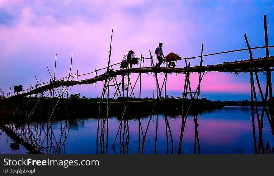 3 Person Walking on Bridge Under Cloudy Sky during Sunrise