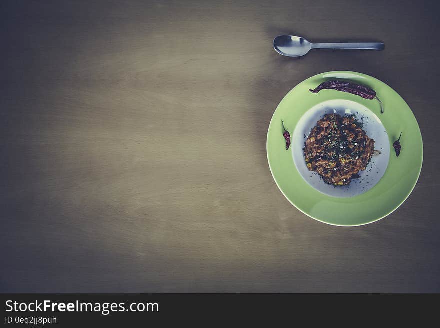 Green and White Ceramic Plate Beside Stainless Steel Spoon on Brown Table