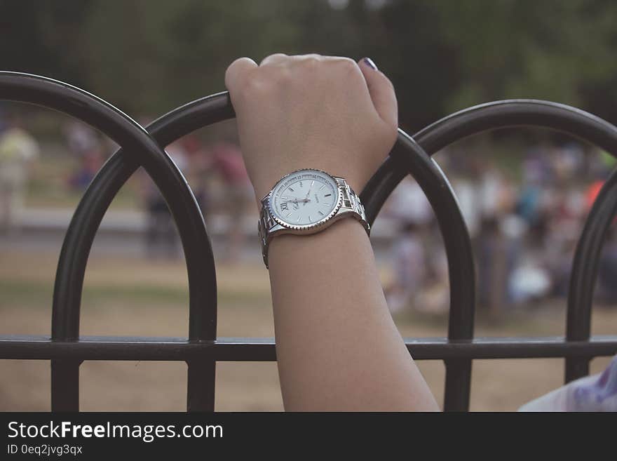 Closeup of woman's hand with watch on her wrist holding painted black metal railings. Closeup of woman's hand with watch on her wrist holding painted black metal railings