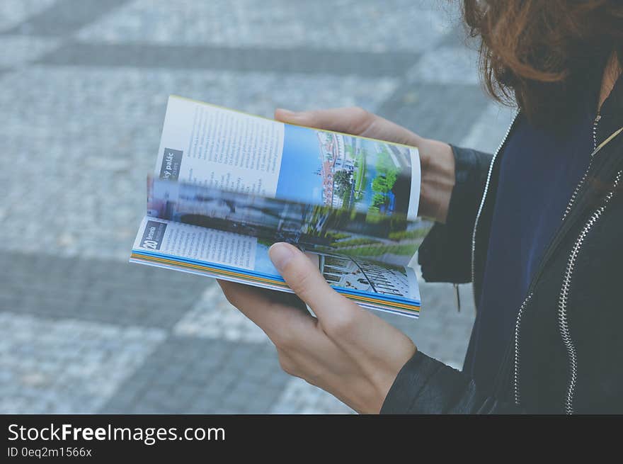 Woman in Black Zipped Jacket Hoding White and Blue Book