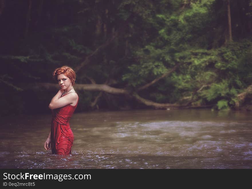 Woman in Red String Spaghetti Strap Dress on Body of Water Near Forest