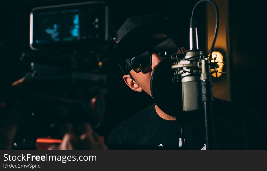 Man in Black Cap and Black Framed Sunglasses in Front Recording Microphone