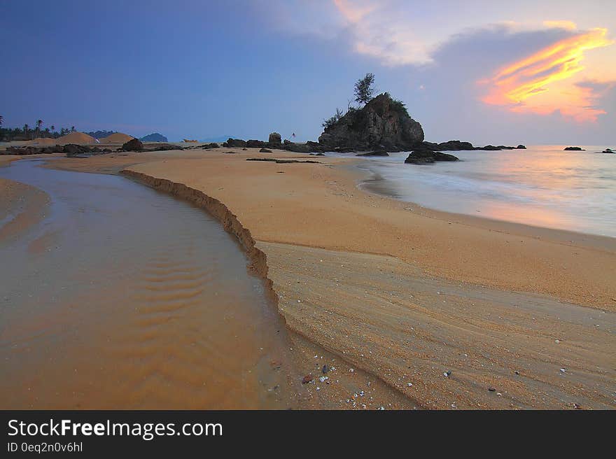 Beach at sunset with receding tide and rocky protrusion with tree growing on it. Beach at sunset with receding tide and rocky protrusion with tree growing on it.