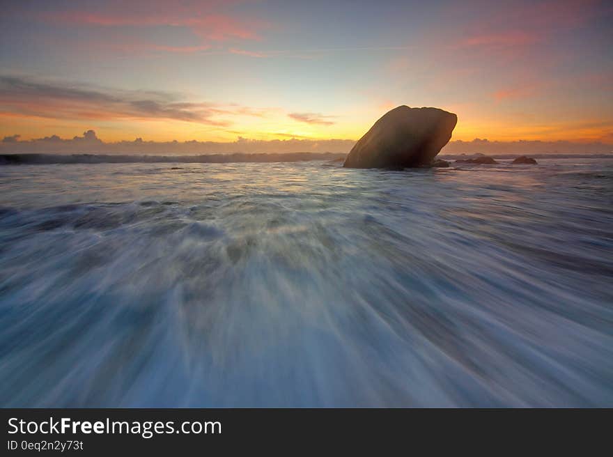 Incoming tide flowing over the beach at dawn with a golden sunrise and a large black rock sticking out above the water. Incoming tide flowing over the beach at dawn with a golden sunrise and a large black rock sticking out above the water.