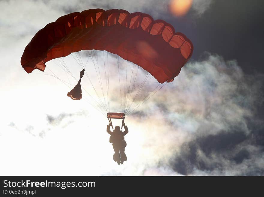 A silhouette of a person parachuting in cloudy sky.