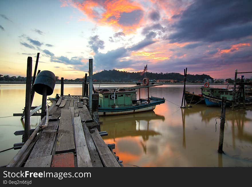 Rickety wooden jetty with fishing boats and beautiful pastel colored sunset reflected in a calm tranquil sea, distant forest over the water. Rickety wooden jetty with fishing boats and beautiful pastel colored sunset reflected in a calm tranquil sea, distant forest over the water.