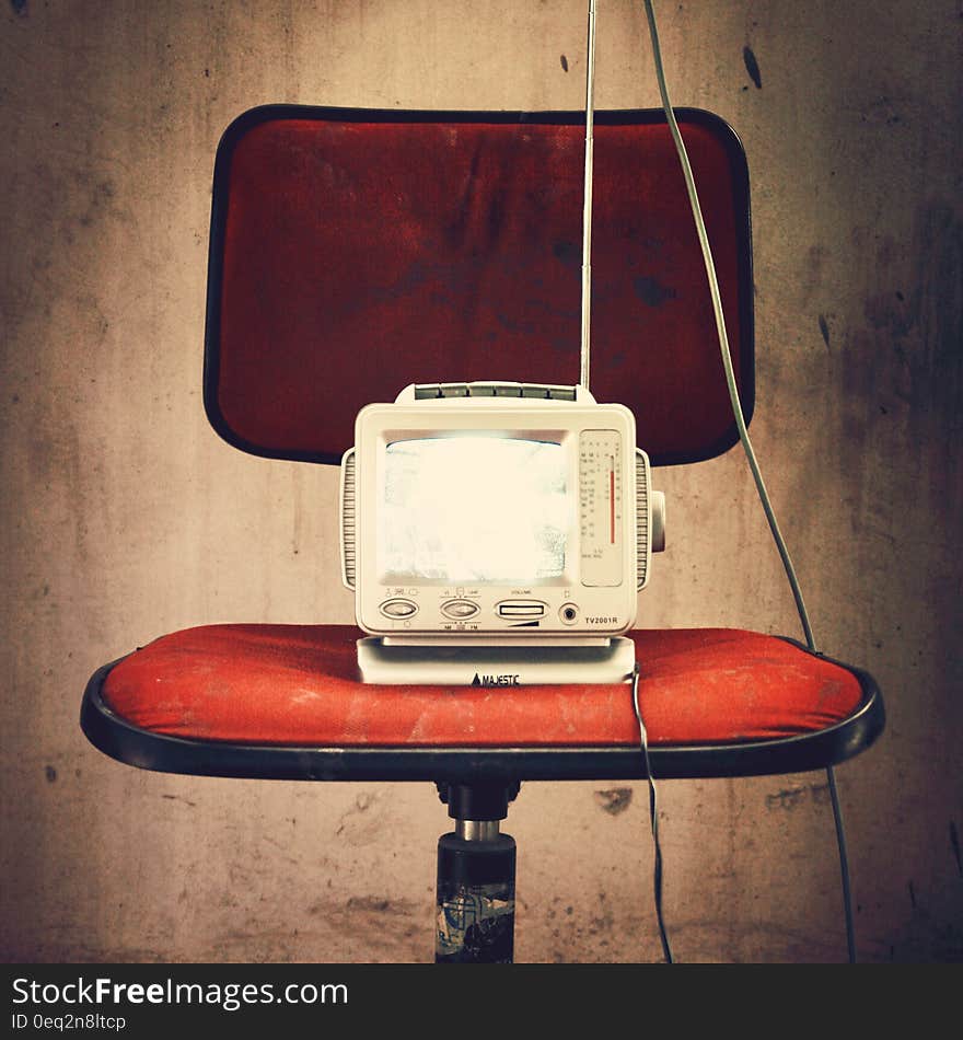 An old fashioned model of a TV on a red chair. An old fashioned model of a TV on a red chair.