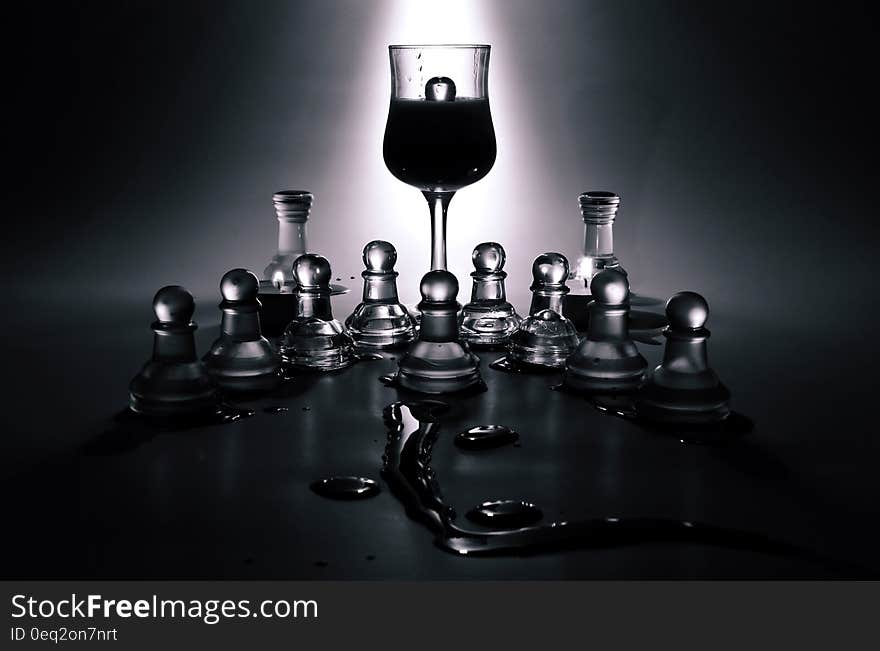 A wine glass standing in the middle of glass chess pieces. A wine glass standing in the middle of glass chess pieces.