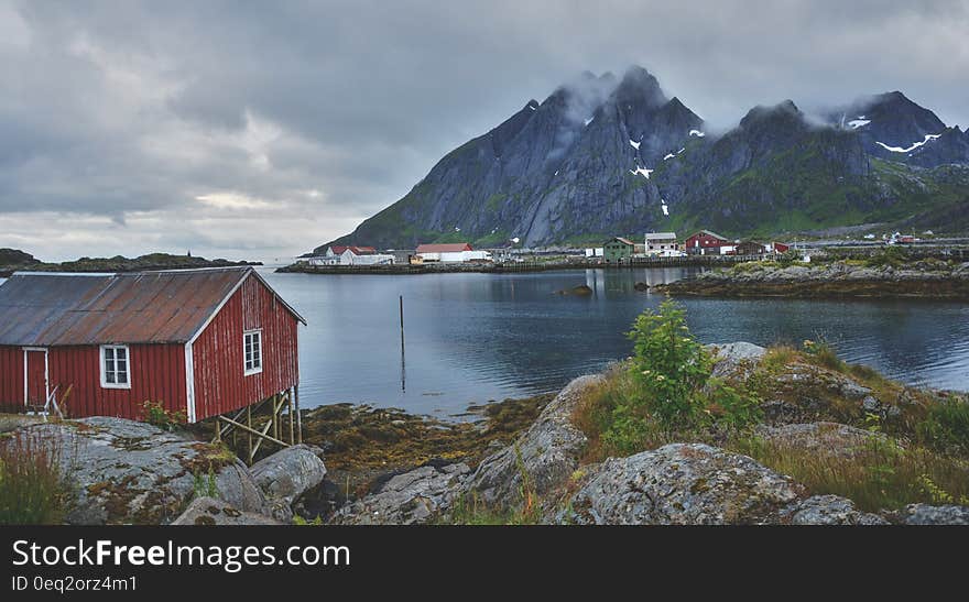 Red Wooden House Near a Mountain and River during Daytime