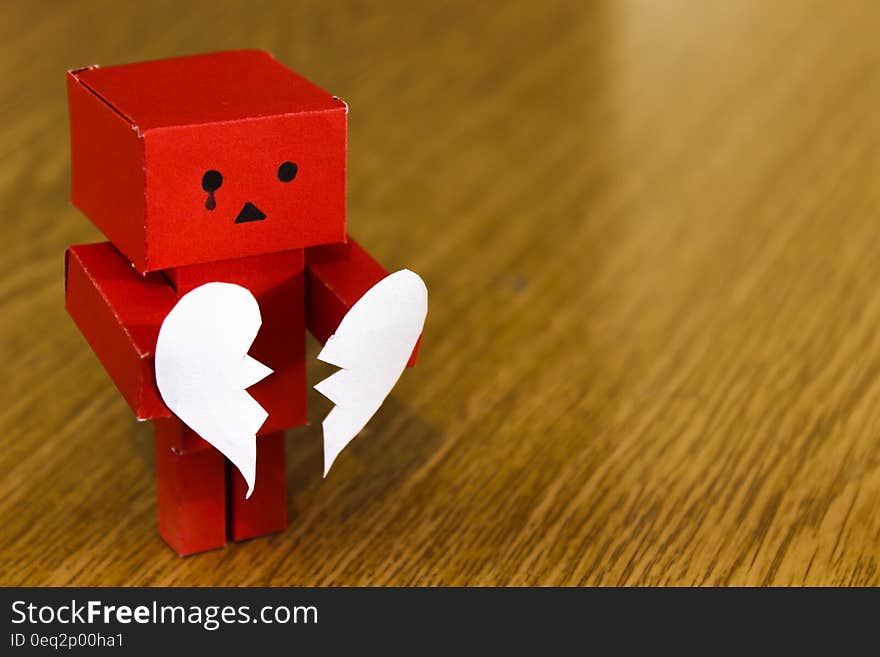 Crying red cardboard model holding broken love heart on wooden background with copy space. Crying red cardboard model holding broken love heart on wooden background with copy space.