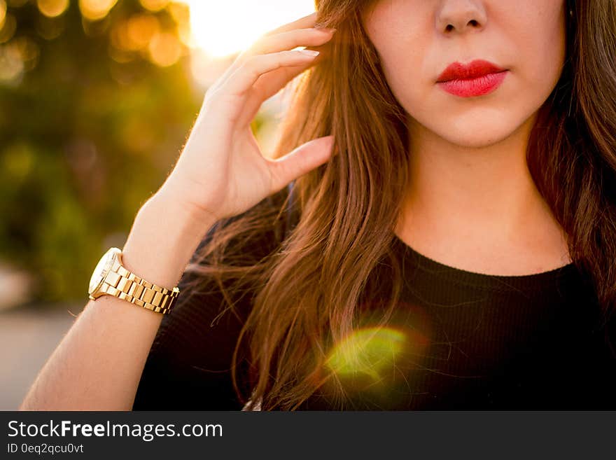 Lower face of beautiful young woman with red lipstick wearing wristwatch outdoors.