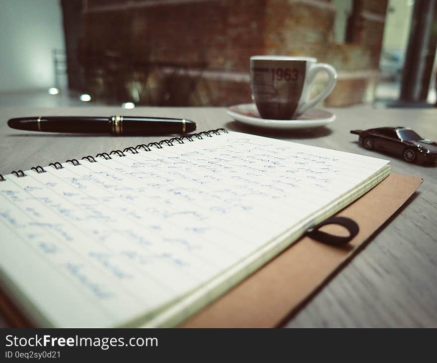 Closeup Photo of Blue Pen Tinted Spiral Notepad Placed Beside Pen Die Cast Car and Coffee Cup