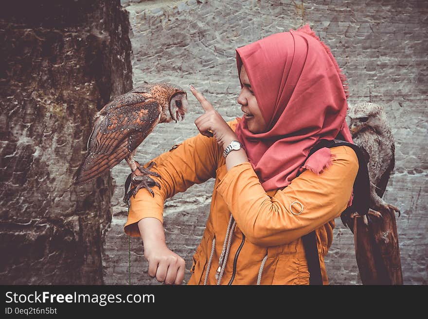 Woman in Red Hijab and Orange Coat Touching Brown and White Owl