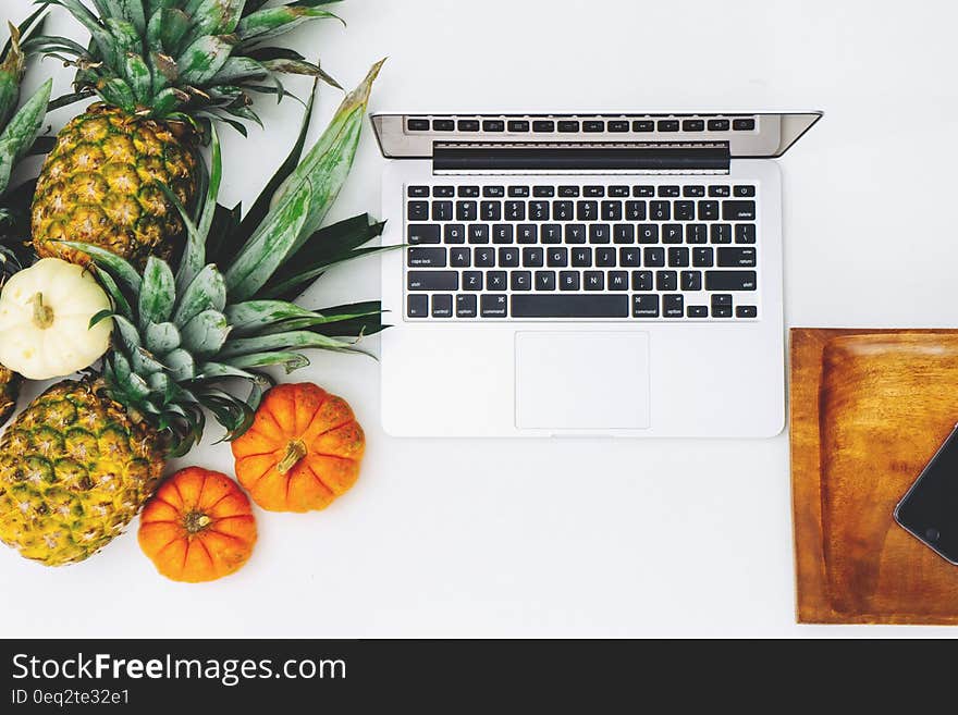 White Macbook Near Pineapple and Pumpkin