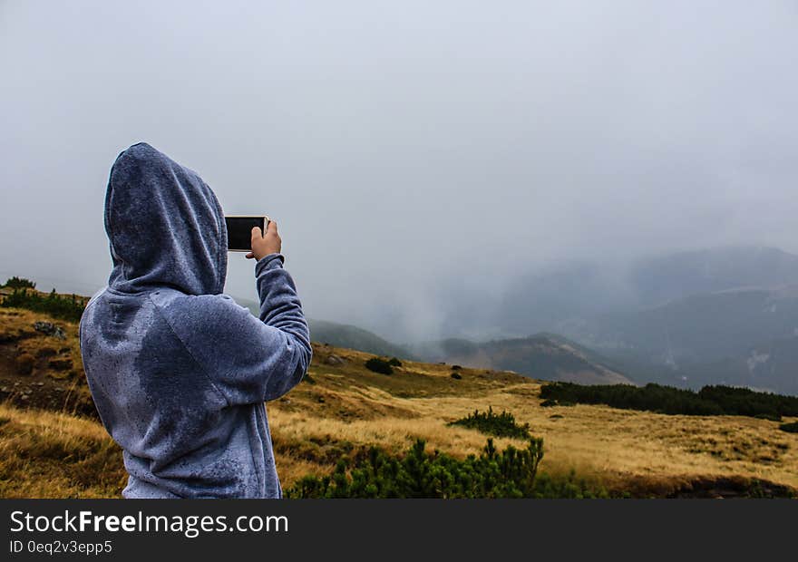 A person with a wet sweater taking a photo of a rainy landscape. A person with a wet sweater taking a photo of a rainy landscape.