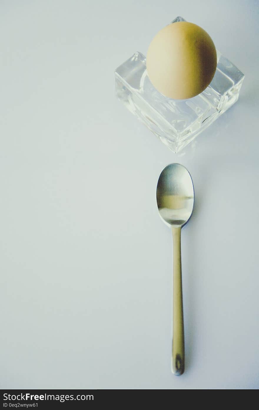 Stainless Steel Spoon Beside Yellow Egg on Clear Glass Fragment