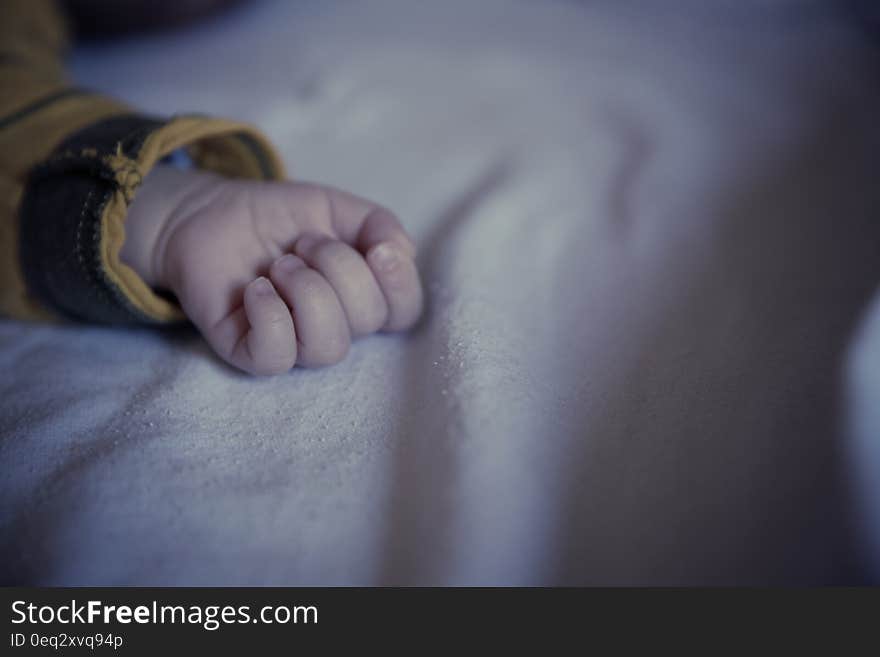 Baby in Yellow and Black Long Sleeved Shirt Lying on White Textile