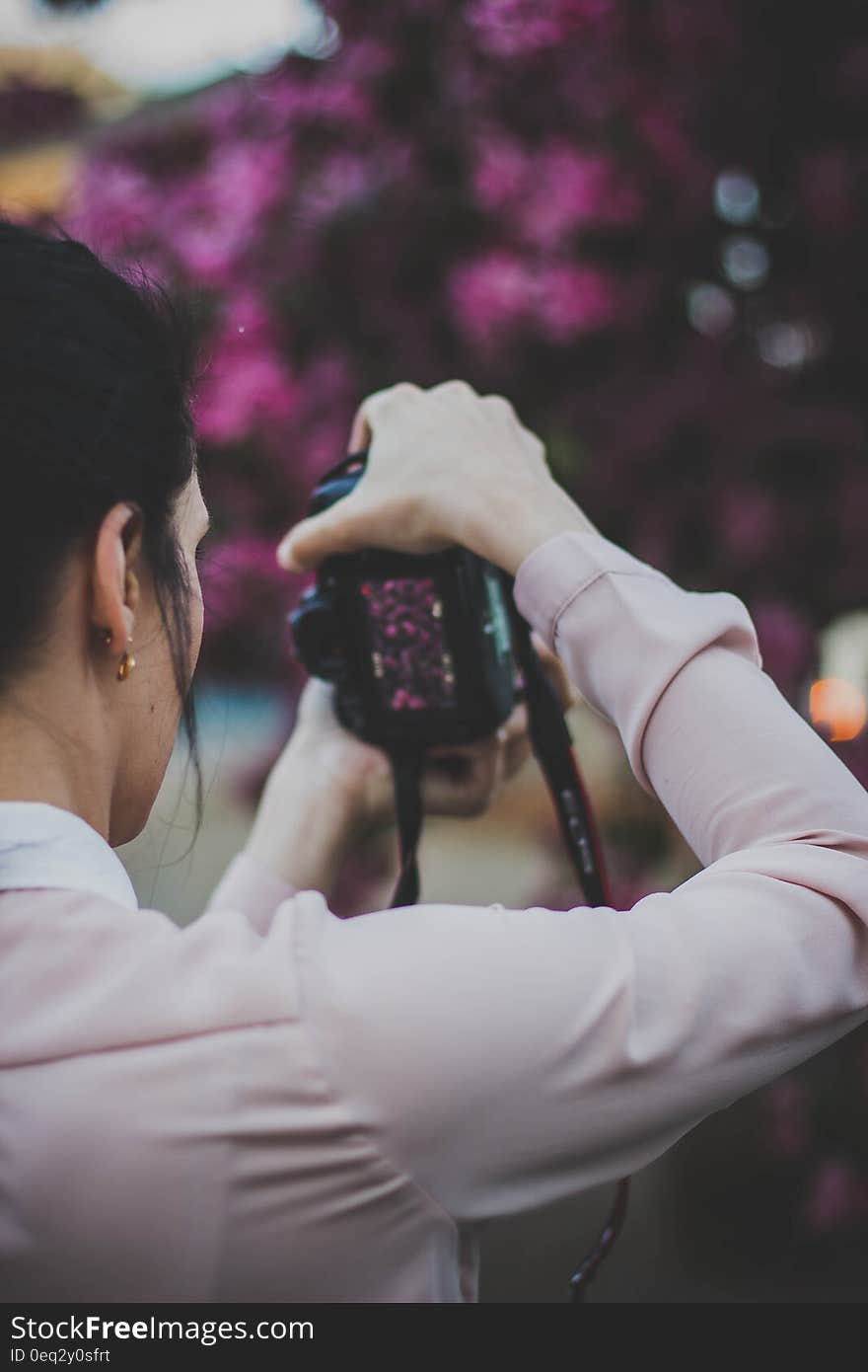 Young woman with camera taking photos of a flowering tree.