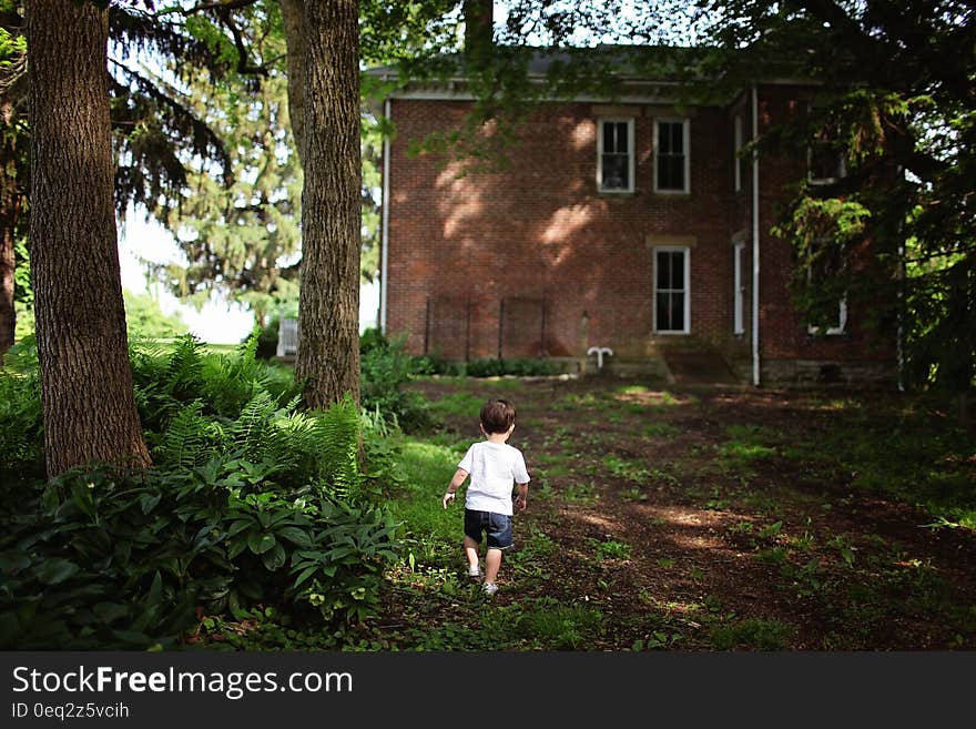 Boy Wearing White Crew Neck T Shirt and Blue Denim Shorts Walking Towards Brown Concrete Building