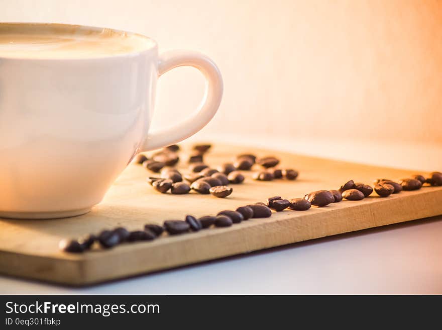 White Ceramic Coffee Mug With Cream Beside Black Coffee Beans