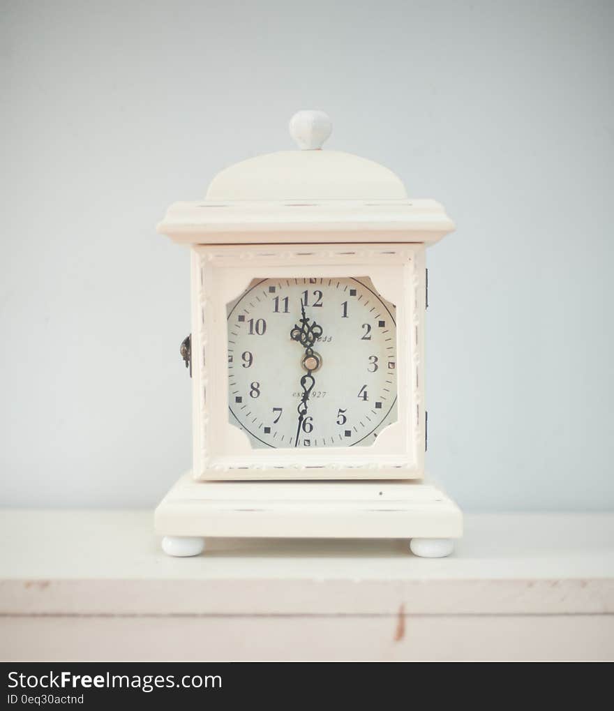 A white antique clock situated on a shelf. A white antique clock situated on a shelf