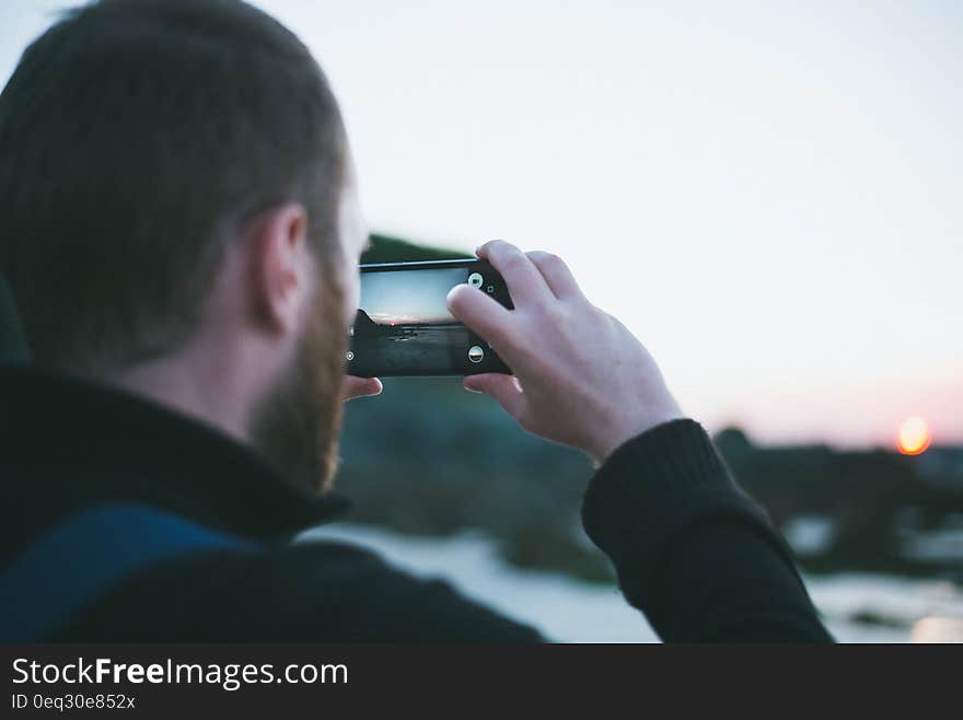 Man at the seaside snaps pictures of sunset with his smartphone. Man at the seaside snaps pictures of sunset with his smartphone