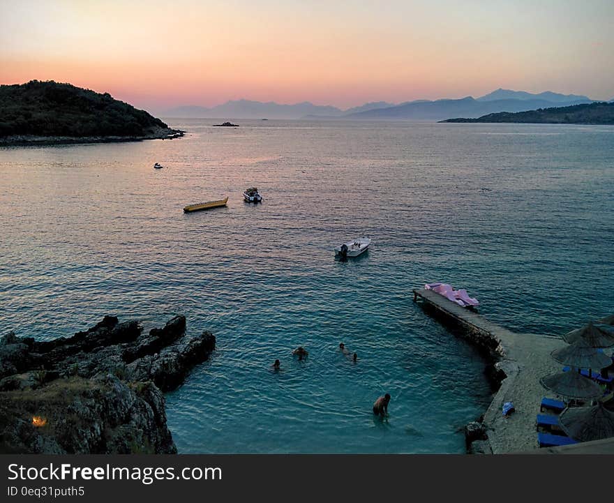 People Swimming in Sea Near Mountain Rocks