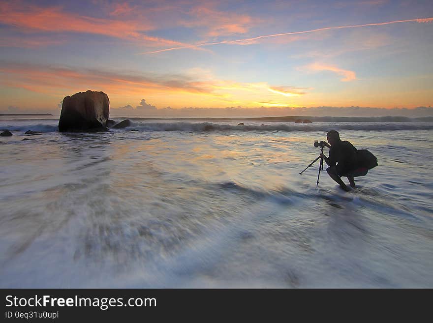 Photographer shooting sunset at the seaside with camera on tripod in the water