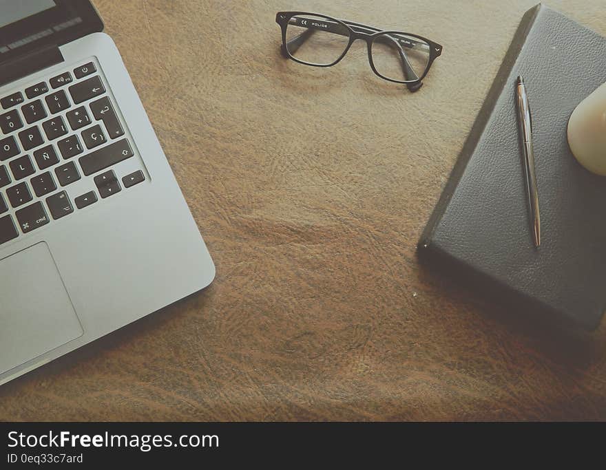 Macbook Pro Beside Black Framed Eyeglasses on Brown Wooden Surface