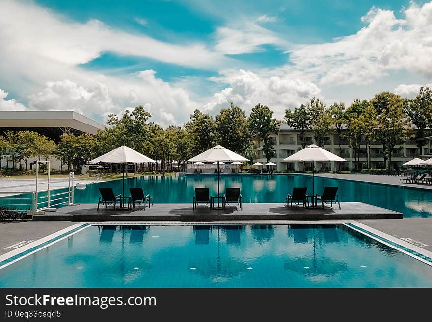 Black Outdoor Lounge Chair in Between Blue Swimming Pool Under White Cloudy Blue Sky