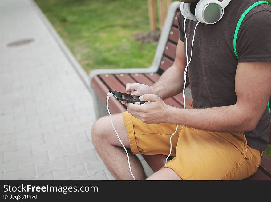 A man sitting on a bench with headphones and checking his mobile phone. A man sitting on a bench with headphones and checking his mobile phone