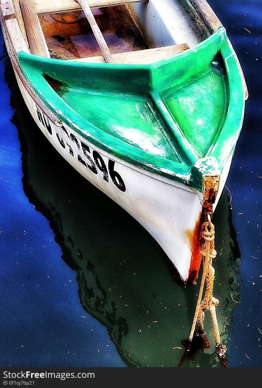 Close up of the bow of a wooden boat painted green and white moored in water. Close up of the bow of a wooden boat painted green and white moored in water.