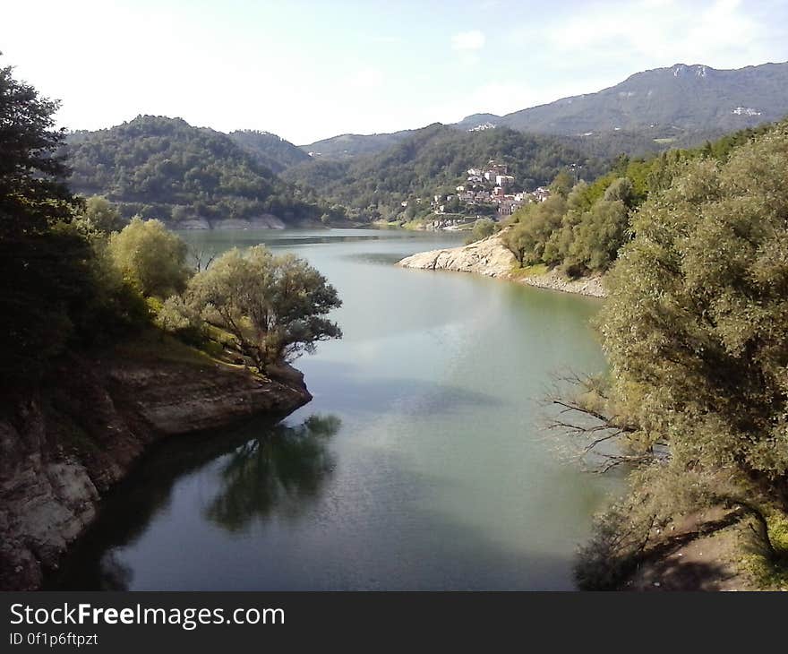 Tranquil meandering river with thick forest on left and right banks and small hamlet (village) downstream, pale gray sky. Tranquil meandering river with thick forest on left and right banks and small hamlet (village) downstream, pale gray sky.